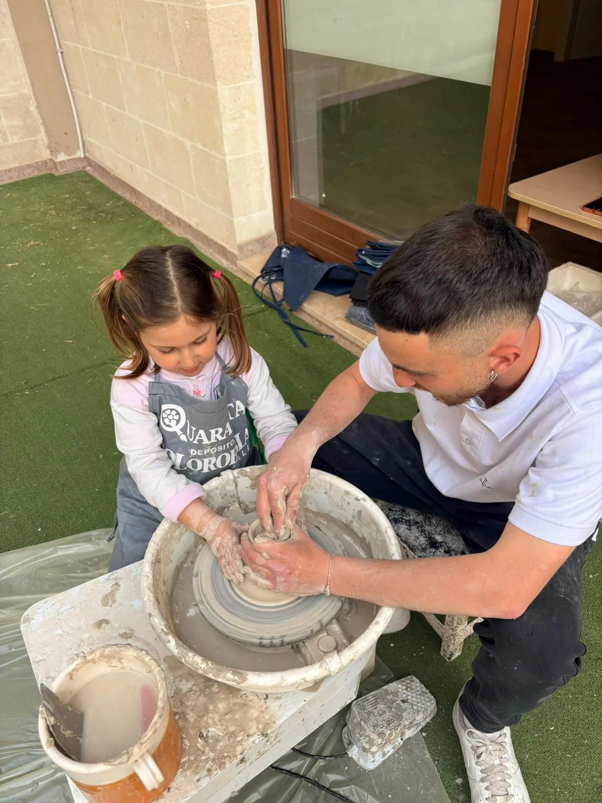 Un maestro guida le mani di una bambina al tornio